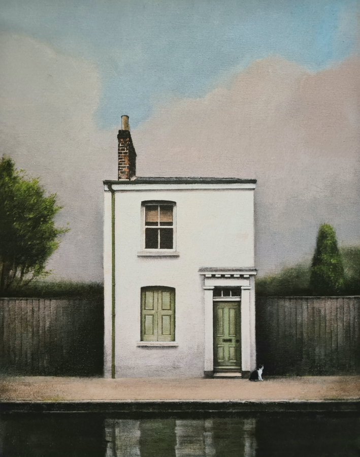 A picturesque white cottage with green doors, set beside a tranquil body of water, accompanied by a black and white cat resting on the ground.